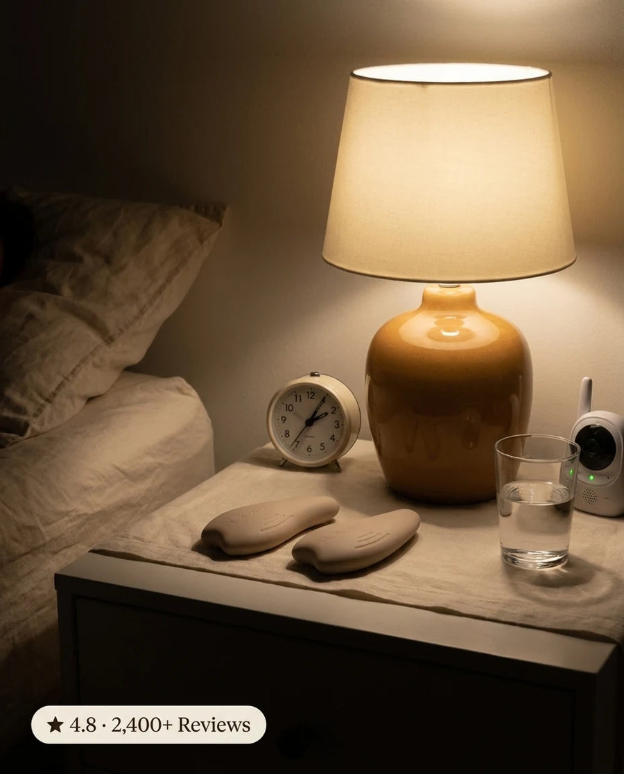 MamaWarm pads resting on a bedside nightstand at night beside a lamp, alarm clock, and baby monitor.